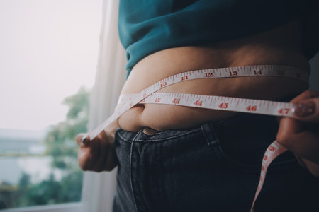 fat woman, fat belly, chubby, obese woman hand holding excessive belly fat with measure tape, woman diet lifestyle conceptの写真素材