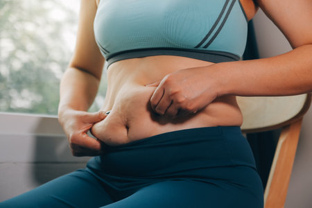 fat woman, fat belly, chubby, obese woman hand holding excessive belly fat with measure tape, woman diet lifestyle conceptの写真素材