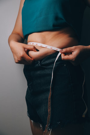 fat woman, fat belly, chubby, obese woman hand holding excessive belly fat with measure tape, woman diet lifestyle conceptの写真素材