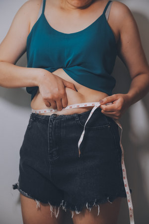 fat woman, fat belly, chubby, obese woman hand holding excessive belly fat with measure tape, woman diet lifestyle conceptの写真素材