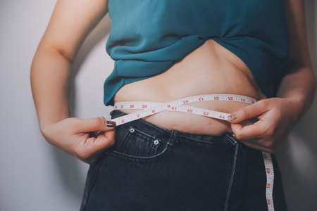 fat woman, fat belly, chubby, obese woman hand holding excessive belly fat with measure tape, woman diet lifestyle conceptの写真素材