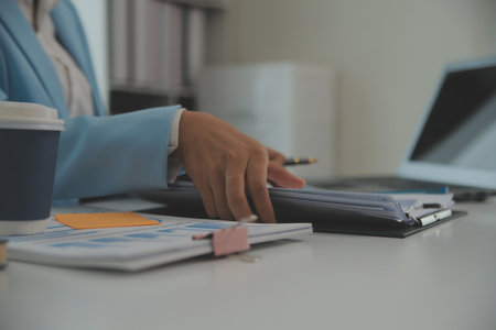 Charming Young asian businesswoman sitting on laptop computer in the office, making report calculating balance Internal Revenue Service checking document.の写真素材