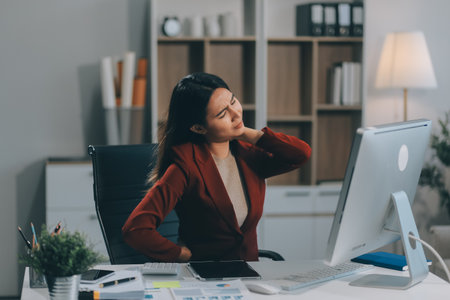 Asian woman working hard in the office having aches and pains in her torso and waistの写真素材
