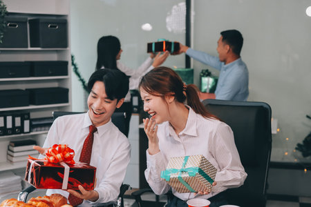 full length view of a group of business team wearing red Santa hat and exchange gift box together in the office for Christmas.の写真素材
