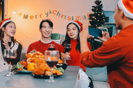 Group of young Asian man and women as friends having fun at a New Year's celebration, holding gift boxes standing by Christmas tree decoration, midnight countdown Party at home with holiday season.の写真素材