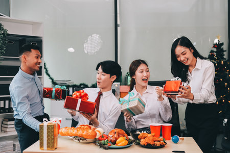 full length view of a group of business team wearing red Santa hat and exchange gift box together in the office for Christmas.の写真素材