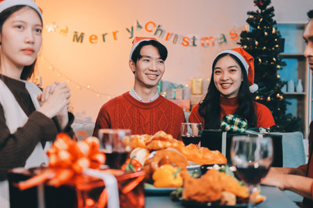 Group of young Asian man and women as friends having fun at a New Year's celebration, holding gift boxes standing by Christmas tree decoration, midnight countdown Party at home with holiday season.の写真素材