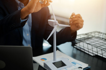 Shut of handsome business man working on new alternative energy development looking at a model of a wind turbine in modern startup.の写真素材
