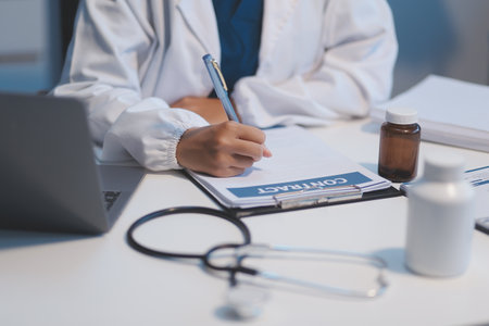 A professional and focused Asian female doctor in scrubs is working and reading medical research on her laptop in her office at a hospital.の写真素材
