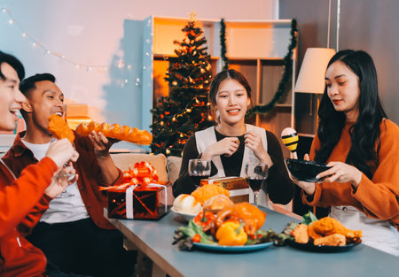 Group of young Asian man and women as friends having fun at a New Year's celebration, holding gift boxes standing by Christmas tree decoration, midnight countdown Party at home with holiday season.の写真素材