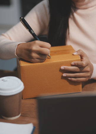 Startup SME small business entrepreneur of freelance Asian woman wearing apron using laptop and box...