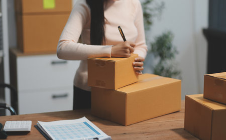 Startup SME small business entrepreneur of freelance Asian woman wearing apron using laptop and box...