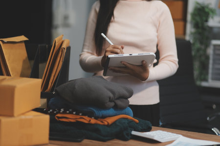 Startup SME small business entrepreneur of freelance Asian woman wearing apron using laptop and box to receive and review orders online to prepare to pack sell to customers, online sme business ideas.の写真素材