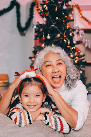 Happy family on Christmas morning. Affectionate grandmother and cheerful granddaughter open a holiday gift together at homeの写真素材