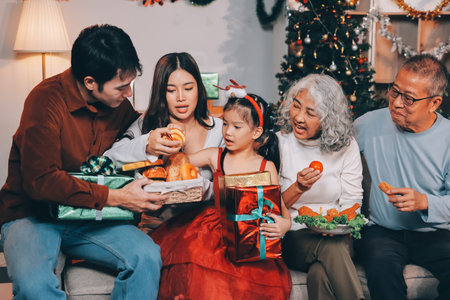 Portrait of Asian family exchanging presents during christmas at home. Attractive happy people holding gift box, celebrate holiday thanksgiving, xmas eve tradition in living room in house together.の写真素材