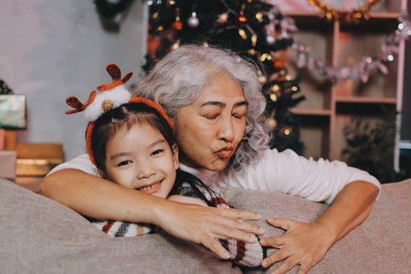 Happy family on Christmas morning. Affectionate grandmother and cheerful granddaughter open a holiday gift together at homeの写真素材
