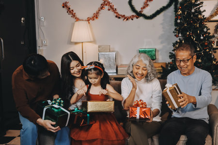 Portrait of Asian family exchanging presents during christmas at home. Attractive happy people holding gift box, celebrate holiday thanksgiving, xmas eve tradition in living room in house together.の写真素材