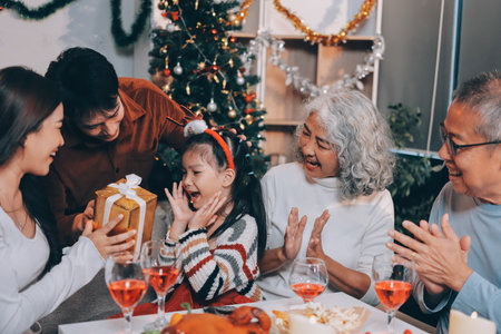 Portrait of Asian family exchanging presents during christmas at home. Attractive happy people holding gift box, celebrate holiday thanksgiving, xmas eve tradition in living room in house together.の写真素材