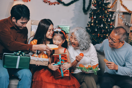 Portrait of Asian family exchanging presents during christmas at home. Attractive happy people holding gift box, celebrate holiday thanksgiving, xmas eve tradition in living room in house together.の写真素材