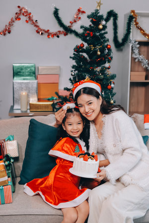 Merry Christmas and Happy Holidays. Cheerful mom and her cute daughter girl exchanging gifts. Parent and little child having fun near tree indoors.の写真素材