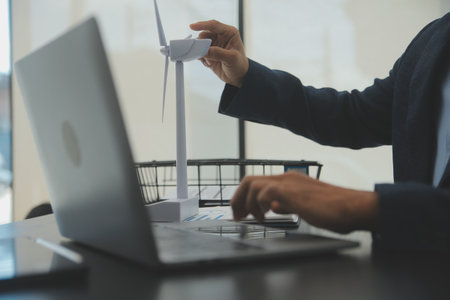 Shut of handsome business man working on new alternative energy development looking at a model of a wind turbine in modern startup.の写真素材