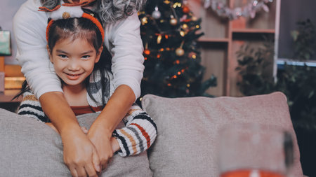 Happy family on Christmas morning. Affectionate grandmother and cheerful granddaughter open a holiday gift together at homeの写真素材
