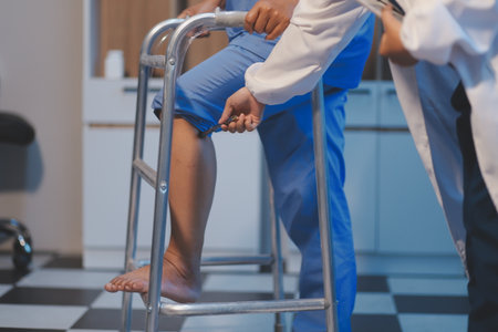Asian young professional successful friendly female nurse in blue hospital uniform helping supporting physical therapy senior old pensioner unhealthy injury woman patient walking via four legs walker.の写真素材