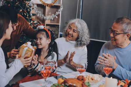 Portrait of Asian family exchanging presents during christmas at home. Attractive happy people holding gift box, celebrate holiday thanksgiving, xmas eve tradition in living room in house together.の写真素材