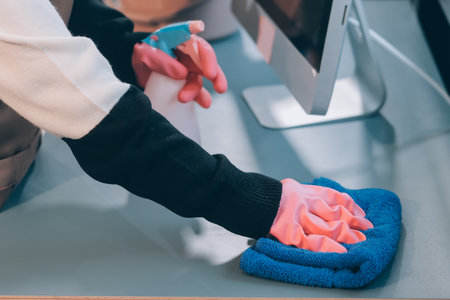 Woman cleaning computer desk in office