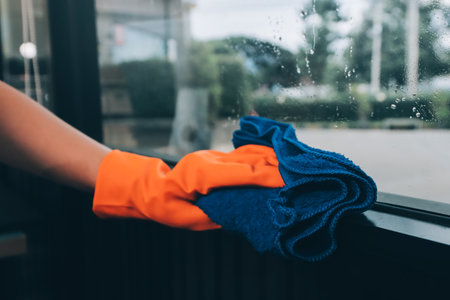 Young female worker cleaning window glass with cloth in spacious villa