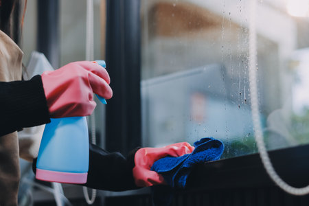An employee of a professional cleaning service in overalls washes the glass of the windows of the...