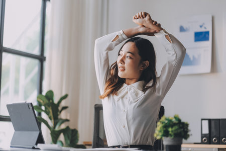 Office asian business woman stretching body for relaxing while working with laptop computer at her desk, office lifestyle, business situationの写真素材