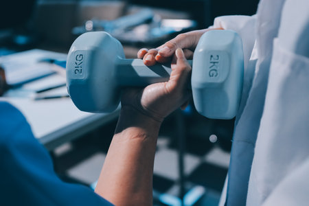 Asian caregiver woman or nurse training senior woman lifting dumbbell for arm exercise while therapy and rehabilitation in living room at home, caretaker or physiotherapist helping elderly workout.の写真素材