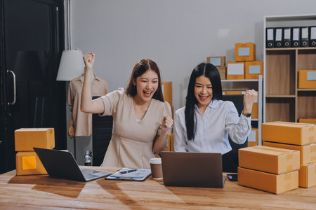 Startup SME small business entrepreneur of freelance Asian woman using a laptop with box Cheerful success Asian woman her hand lifts up online marketing packaging box and delivery SME idea conceptの写真素材
