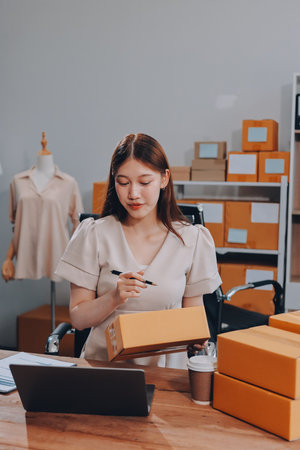 Startup SME small business entrepreneur of freelance Asian woman using a laptop with box Cheerful success Asian woman her hand lifts up online marketing packaging box and delivery SME idea conceptの写真素材