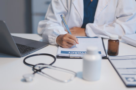 A professional and focused Asian female doctor in scrubs is working and reading medical research on her laptop in her office at a hospital.の写真素材