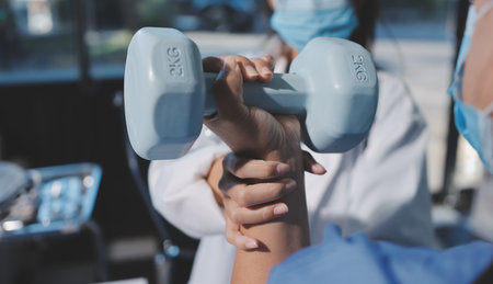 Asian caregiver woman or nurse training senior woman lifting dumbbell for arm exercise while therapy and rehabilitation in living room at home, caretaker or physiotherapist helping elderly workout.の写真素材