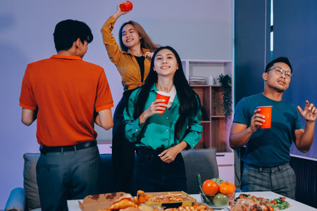 Happy young friends group having lunch at home. Asia family party eating pizza and laughing enjoying meal while sitting at dining table together at house. Celebration holiday and togetherness.の写真素材