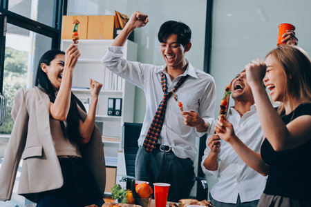Asian office colleagues and friends enjoy a daytime BBQ with pizza and beer, creating a lively atmosphere filled with joy.の写真素材
