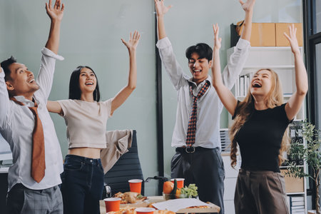 Asian office colleagues and friends enjoy a daytime BBQ with pizza and beer, creating a lively atmosphere filled with joy.の写真素材
