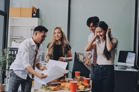 Asian office colleagues and friends enjoy a daytime BBQ with pizza and beer, creating a lively atmosphere filled with joy.の写真素材