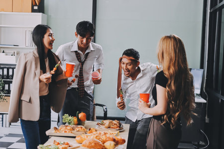 Asian office colleagues and friends enjoy a daytime BBQ with pizza and beer, creating a lively atmosphere filled with joy.の写真素材