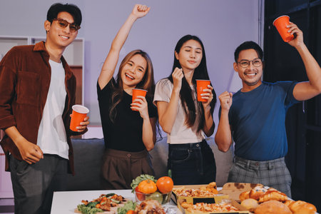 Happy young friends group having lunch at home. Asia family party eating pizza and laughing enjoying meal while sitting at dining table together at house. Celebration holiday and togetherness.の写真素材