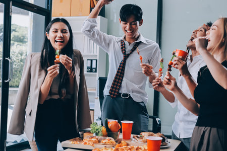 Asian office colleagues and friends enjoy a daytime BBQ with pizza and beer, creating a lively atmosphere filled with joy.の写真素材