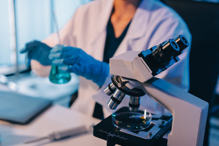 Two women in a lab work on food research, using a microscope, petri dish, and test tubes filled with chemical solutions. They study vegetables, pork, and plants for traits and nutrition.の写真素材