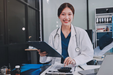Medical health clinic beautiful Asian doctor working using smart tablet touching, stethoscope diagnosing patient analysis research examination healthcare provider service insurance in modern officeの写真素材
