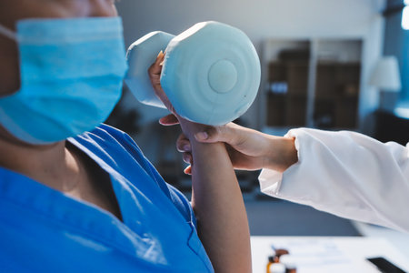 Asian caregiver woman or nurse training senior woman lifting dumbbell for arm exercise while therapy and rehabilitation in living room at home, caretaker or physiotherapist helping elderly workout.の写真素材
