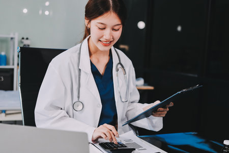 Medical health clinic beautiful Asian doctor working using smart tablet touching, stethoscope diagnosing patient analysis research examination healthcare provider service insurance in modern officeの写真素材