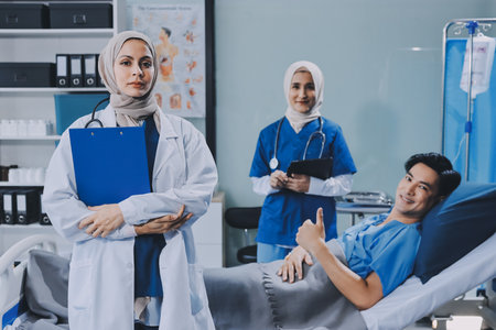 A young man lies on a bed in a hospital ward talking with her young Indian doctor. Doctor checking patient's health doctor treating patient, hospital admission of patientの写真素材
