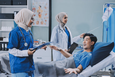 A young man lies on a bed in a hospital ward talking with his doctor. Doctor checking patient's health, doctor treating patient, hospital admission of patientの写真素材
